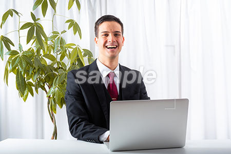 PCをしながらデスクで正面を見て笑うビジネスマン a0010170PH