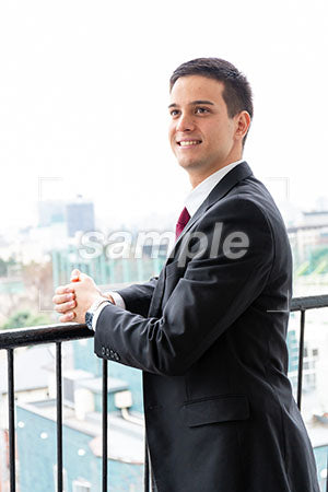 オフィスのベランダで男性が左上を見て微笑む a0010261PH