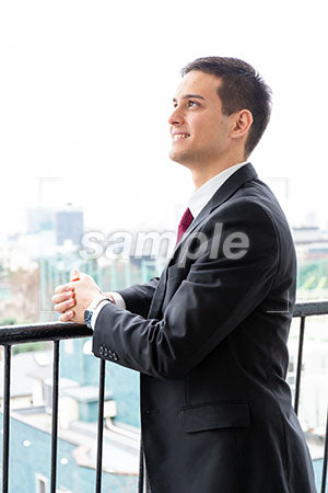 オフィスのベランダで男性が左上を見て微笑む a0010265PH