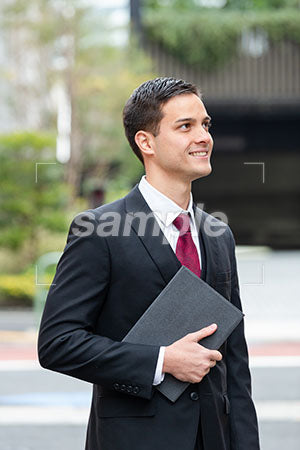 オフィス街でPCをもった男性が右上を見て微笑む a0010365PH