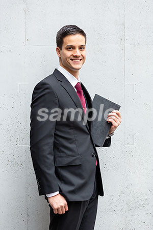 コンクリートの壁をバックにビジネスマンの男性の笑顔の表情　正面を見て微笑む a0010452PH