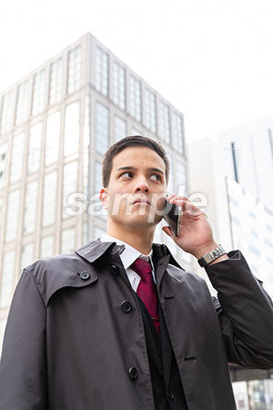 コートを着たビジネスマンが電話で話しながら右を見る a0010553PH