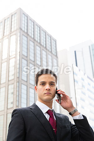 ビル街でスマホで電話しながら正面を見る男の人 a0010561PH