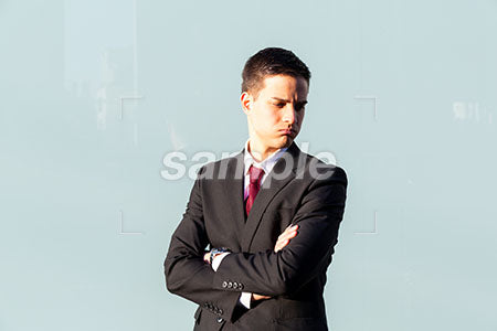 街中でビジネスマンの男性の悲しい表情 腕を組んで右下を見て悲しむ a0010829PH