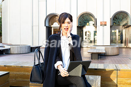 屋外の広場でコートを着た女性が顔に手を添えて驚く a0020523PH