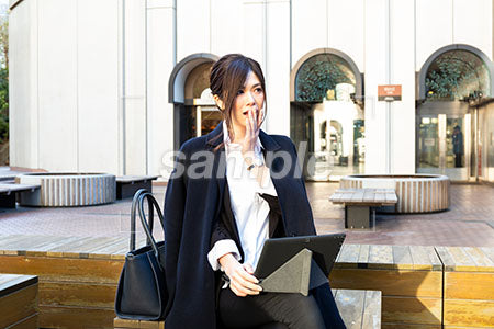 屋外の広場でコートを着た女性が口に手を当てて驚く a0020526PH