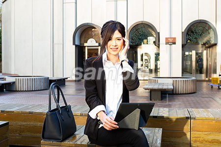 昼休みに外で仕事をしている女性が側頭部に手を添えて微笑む a0020535PH