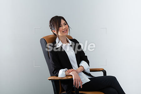ブラックスーツの女性が椅子にこしかけ笑顔で右上を見る a0020964PH