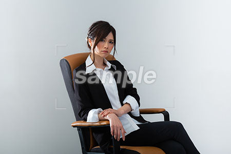 ブラックスーツの女性が椅子にこしかけ怒って正面を見る a0020965PH
