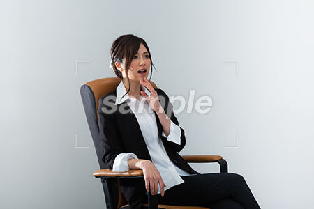 椅子に座って口に手を当てて驚くスーツの女性 a0020976PH