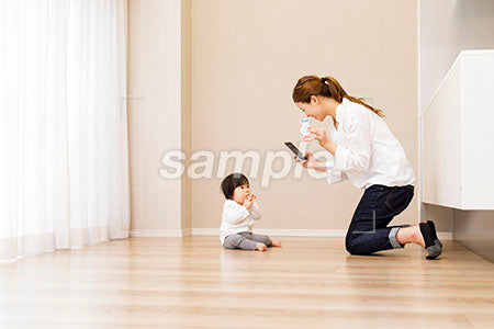 床に座る赤ちゃんをスマホで撮るママ a0030368PH