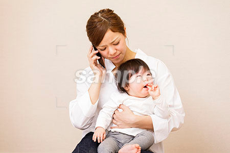 泣く赤ちゃんを抱っこして電話する母親 a0030402PH