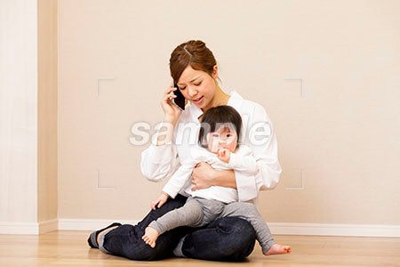 泣く赤ちゃんを抱っこしてスマホで電話する母親 a0030403PH
