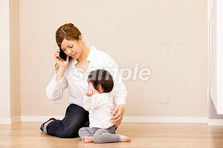 泣く赤ちゃんの背中に手を当てて電話する若いママ a0030410PH