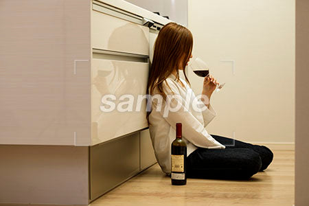 料理をしながらキッチンの床に座って赤ワインを飲む女性 a0030421PH
