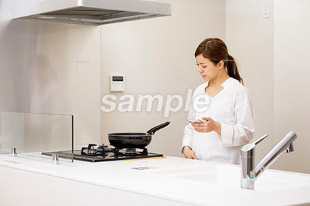 スマホ片手にキッチンに立つ女性 a0030432PH