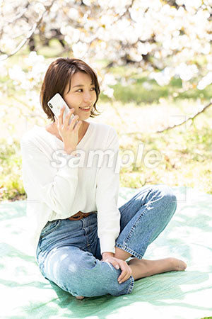 桜の下で電話するあぐらで座る女性 a0050174PH
