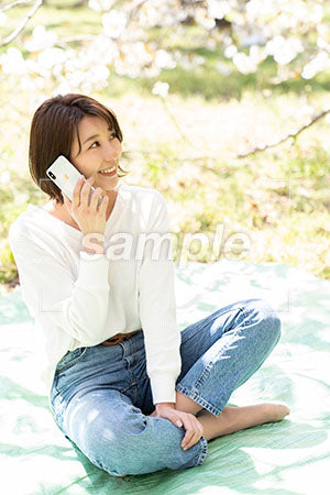 桜の下で電話する女性 右上を見る a0050175PH