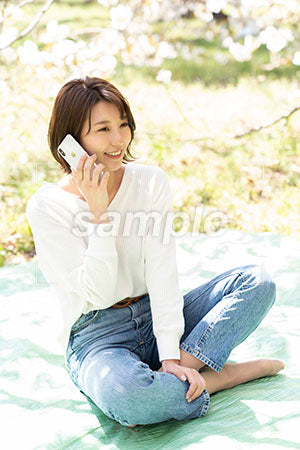 お花見の桜の下で電話する胡座ですわる女性 a0050177PH