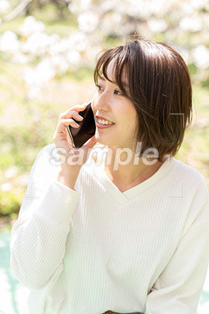 桜の下で電話で話している左を見る女性 a0050180PH