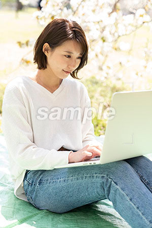 屋外で仕事をする、膝の上にパソコンをする女性 a0050190PH