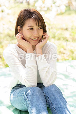 体育座りで桜の下で両ほほに手をあてて笑顔の女性の真 a0050195PH
