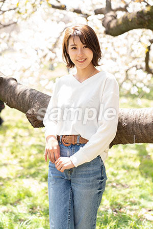 桜の下に立つ女性が枝の前に立って正面を見る a0050212PH