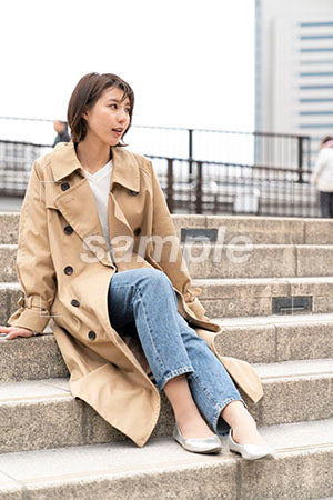コートを着た女性が階段に座って右を見る a0050403PH