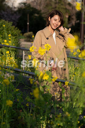 菜の花越しの茶色いコートを女性 正面を見る a0050598PH