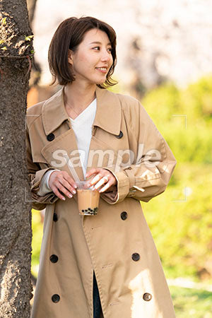 木に寄りかかってタピオカドリンクを持つ女性が右を見る a0050647PH