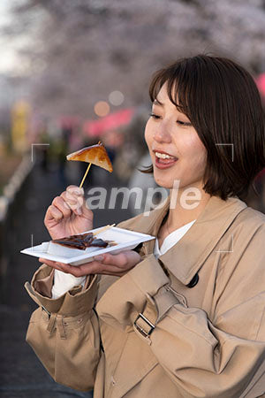 春の花見で食べ物を食べるスプリングコートを着た女性が手元を見る a0050715PH