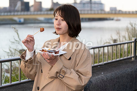 花見で食べ物を食べるスプリングコートを着た女性 手元を見る a0050724PH