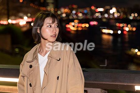 夜の川沿いに佇むスプリングコートを着た女性 右を見る a0050728PH