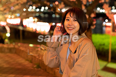 夜桜とスプリングコートの女性 座りながら笑顔で正面を見る a0050755PH